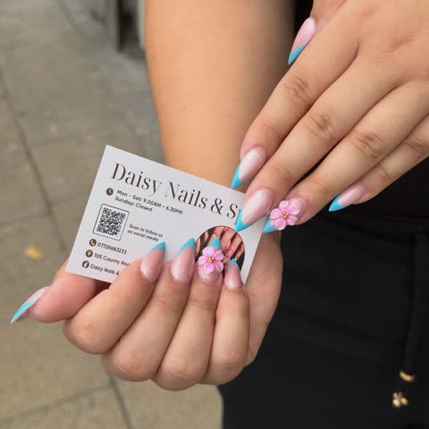 Client with pink floral tips holding a Daisy Nails business card