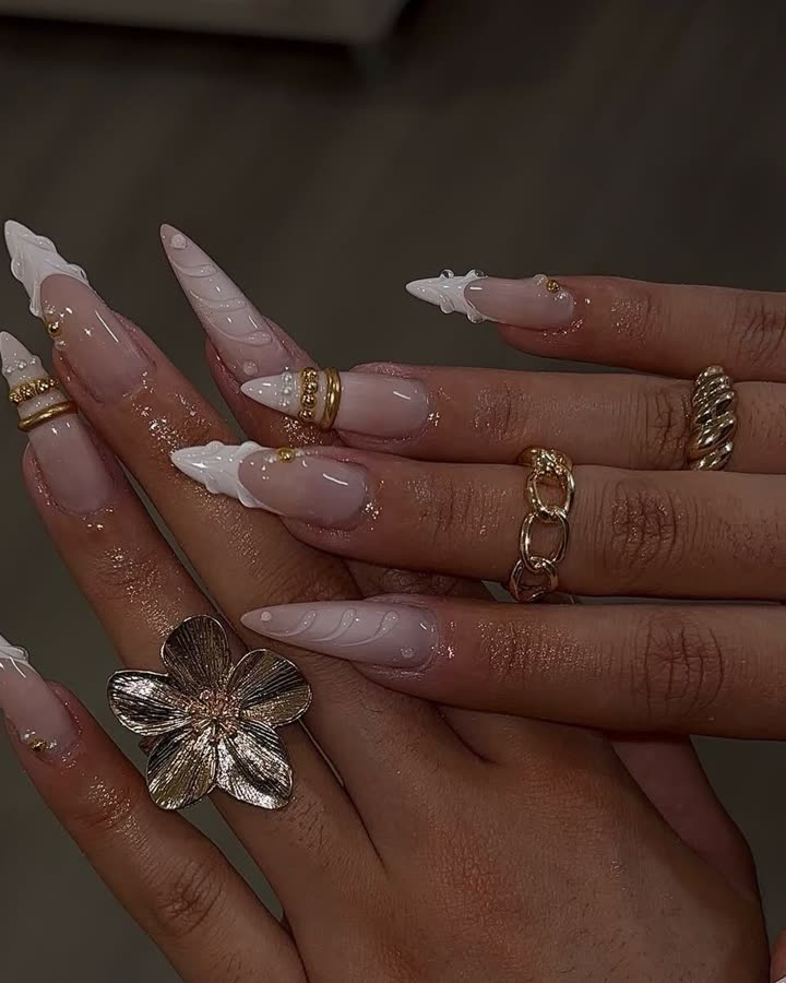 Pearl-white stiletto nails with gold accents and a flower ring